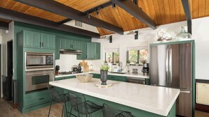 Una cucina moderna con mobili verdi, una grande isola, sgabelli da bar, un frigorifero in acciaio inossidabile e un forno a microonde.