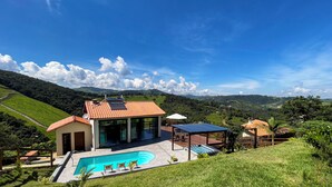 A modern house with a swimming pool, solar panels, and a view of the surrounding hills.