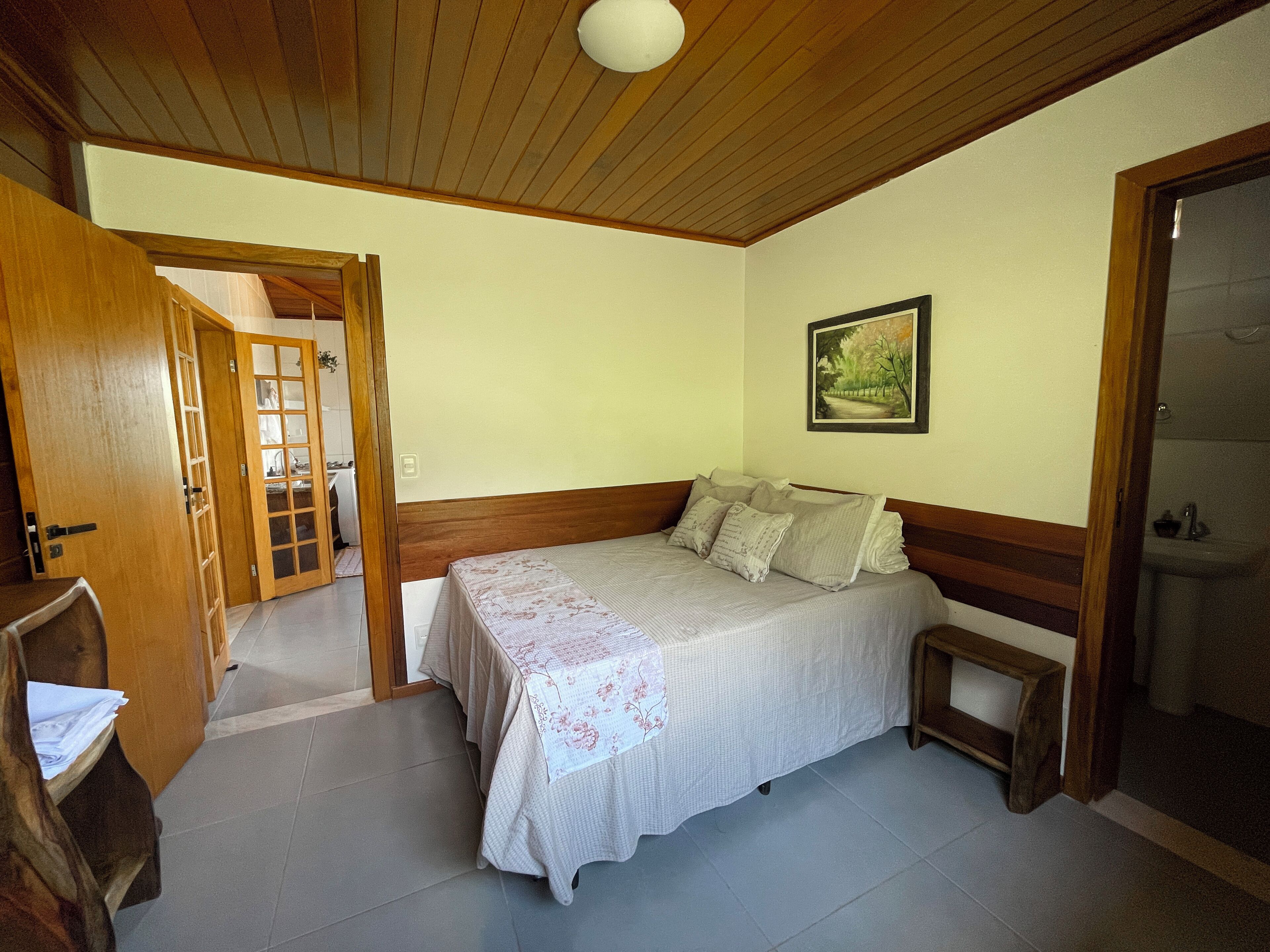 Une chambre avec un plafond en bois, un lit recouvert d’une couvre-lit à motifs floraux, une table de chevet et un tableau accroché au mur.