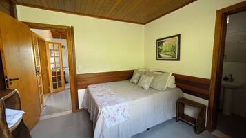 Une chambre avec un plafond en bois, un lit recouvert d’une couvre-lit à motifs floraux, une table de chevet et un tableau accroché au mur.
