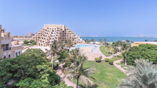 Un hotel con piscina, palmeras y vistas al mar.