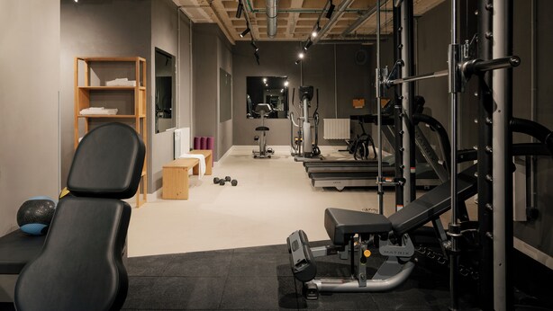 Een sportschool met trainingsapparatuur, een bank, een loopband en een spiegelwand.