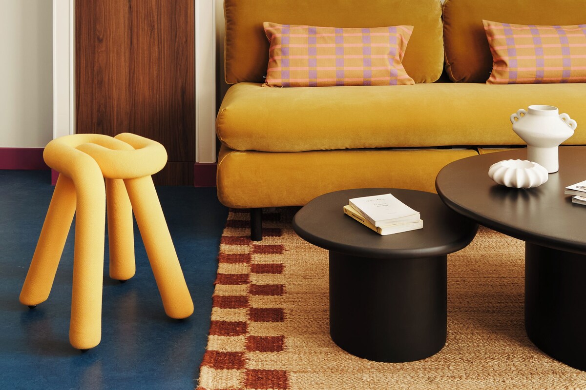 A modern living room with a mustard sofa, a black coffee table, and a yellow stool.