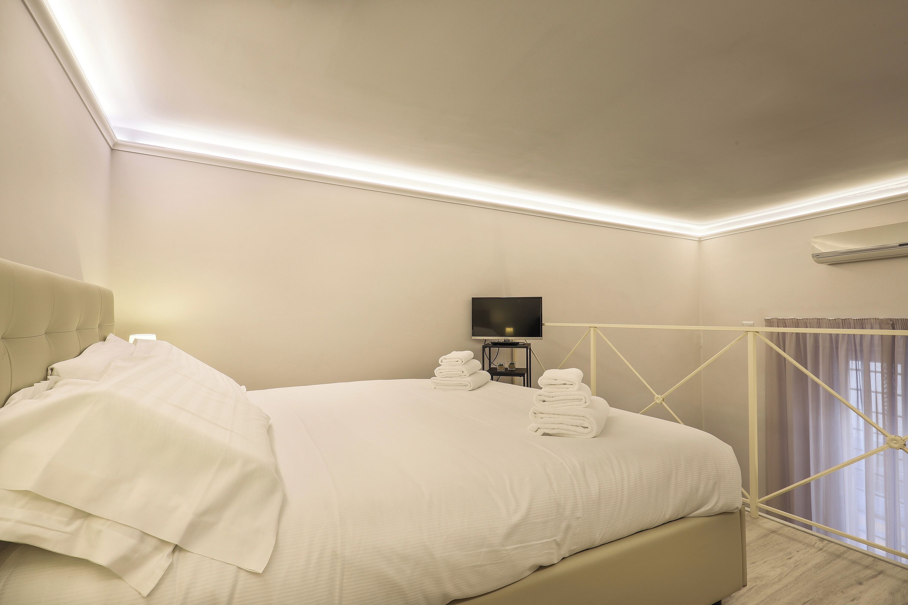A neatly made bed with white linens and towels, a bedside table with a lamp, and a large window with curtains.