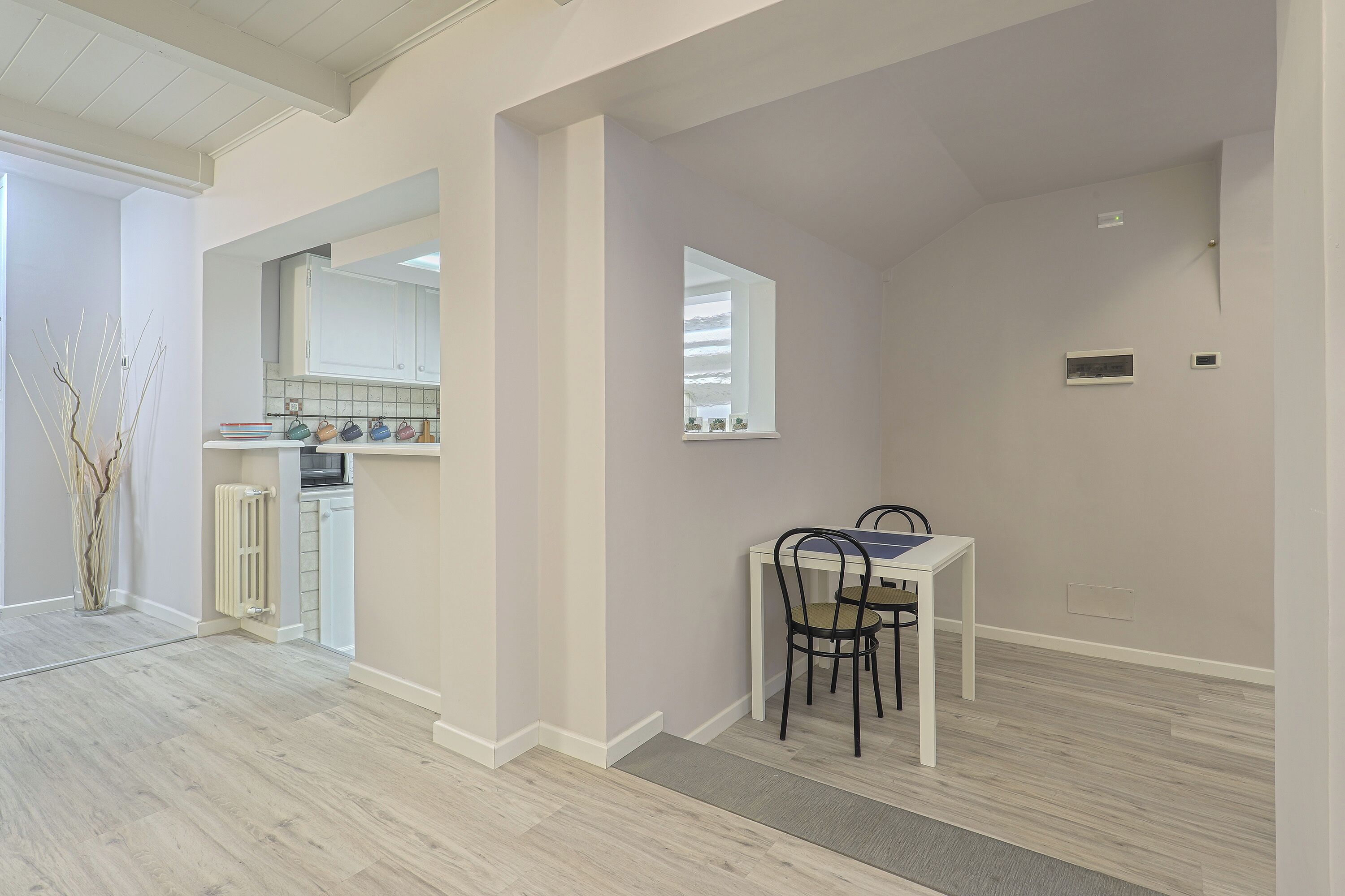 A modern kitchen with white cabinets, a built-in oven, and a dining area with a white table and two chairs.