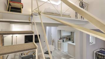 A multi-level interior with a staircase, a living area with a sofa, a dining table, and a kitchen area.