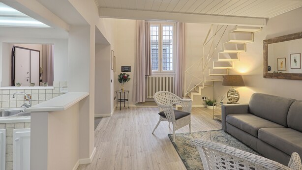 A modern living room with a staircase, a sofa, and a dining area with a kitchen in the background. - Giglio Bianco (Florence)