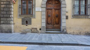 A building facade with a large wooden double door, a window with metal bars, and a stone wall. - Giglio Bianco (Florence)