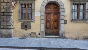Fachada de edificio con un gran puerta doble de madera, una ventana con barrotes de metal y un muro de piedra.