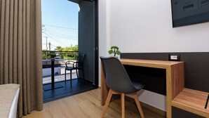 Een moderne hotelkamer met een houten bureau, een zwarte stoel, een kleine potplant en een groot raam met uitzicht op de omgeving.