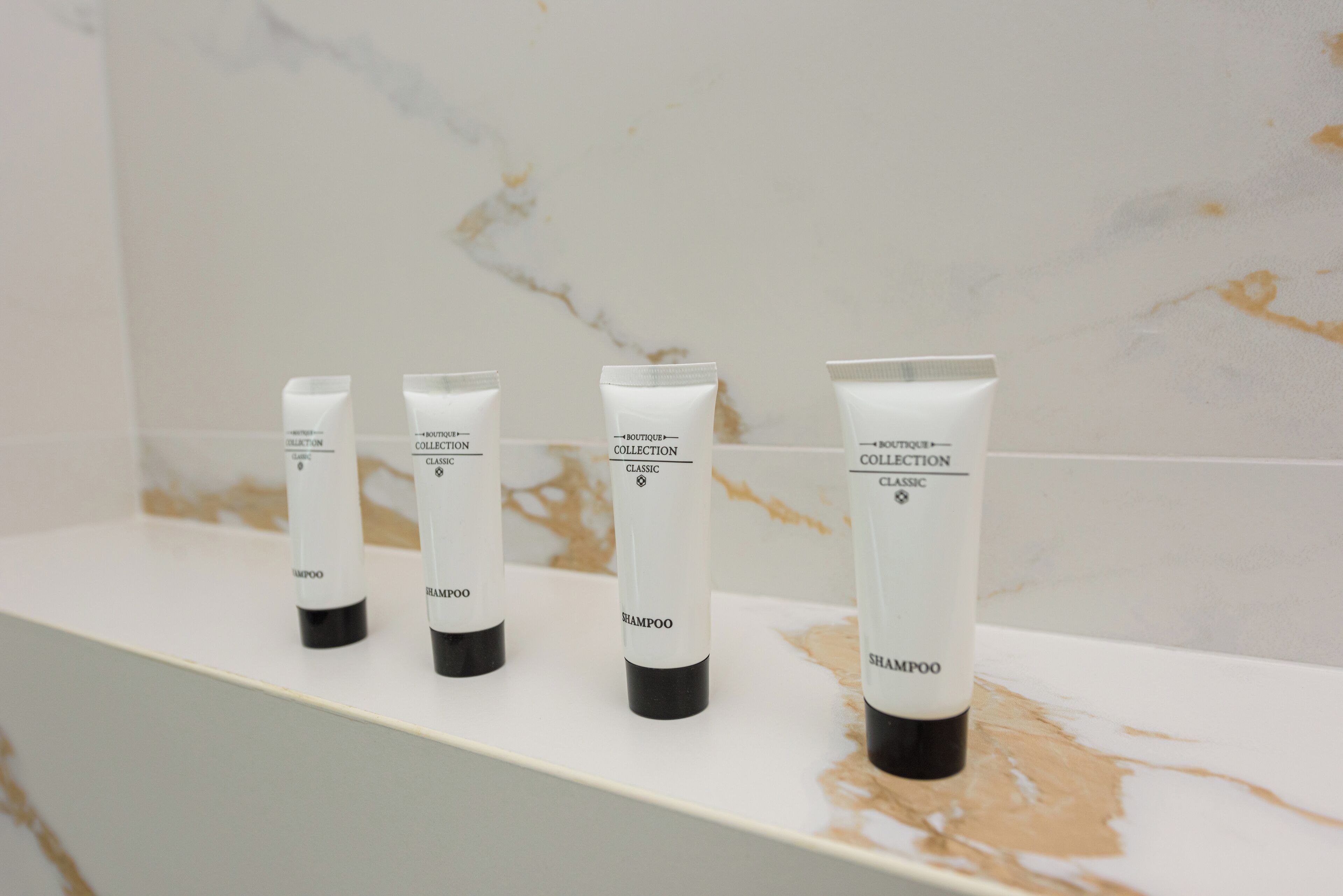 Vier Shampoo-Flaschen auf einem weißen Regal vor einer Marmorwand.
