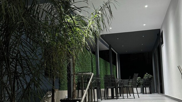 Een modern gebouw met een trap die leidt naar een overdekt gebied. Er staan potplanten en is zitgelegenheid buiten.