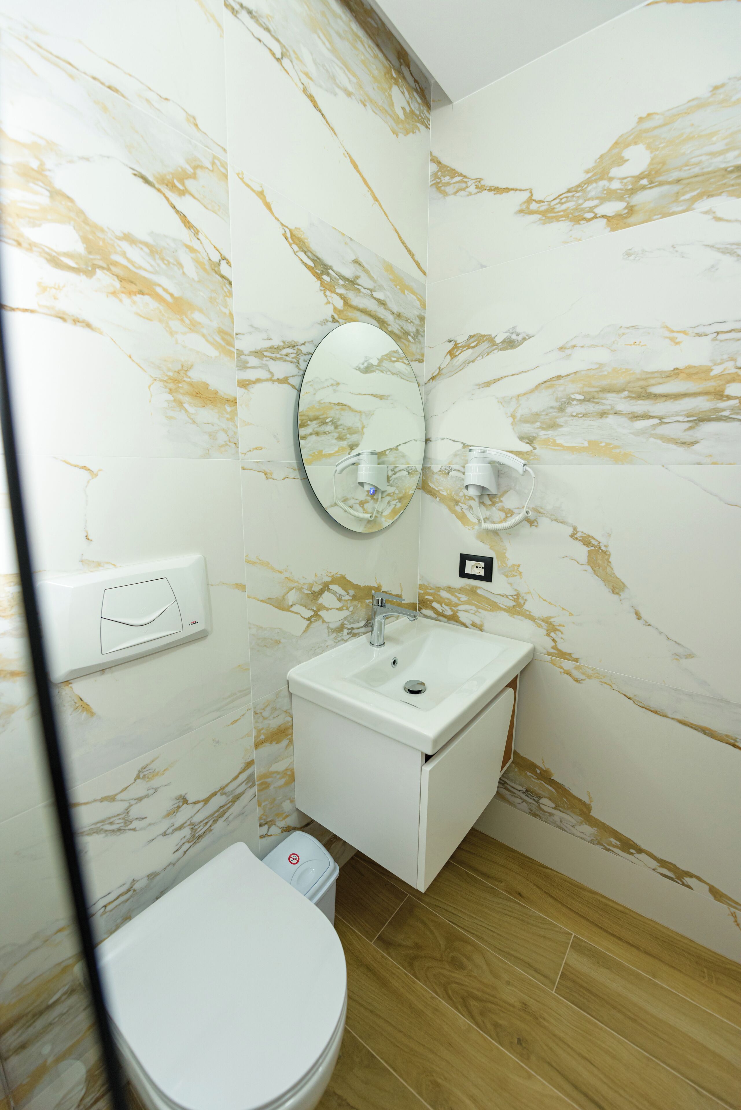 A bathroom with a marble wall, a sink, a mirror, and a toilet.