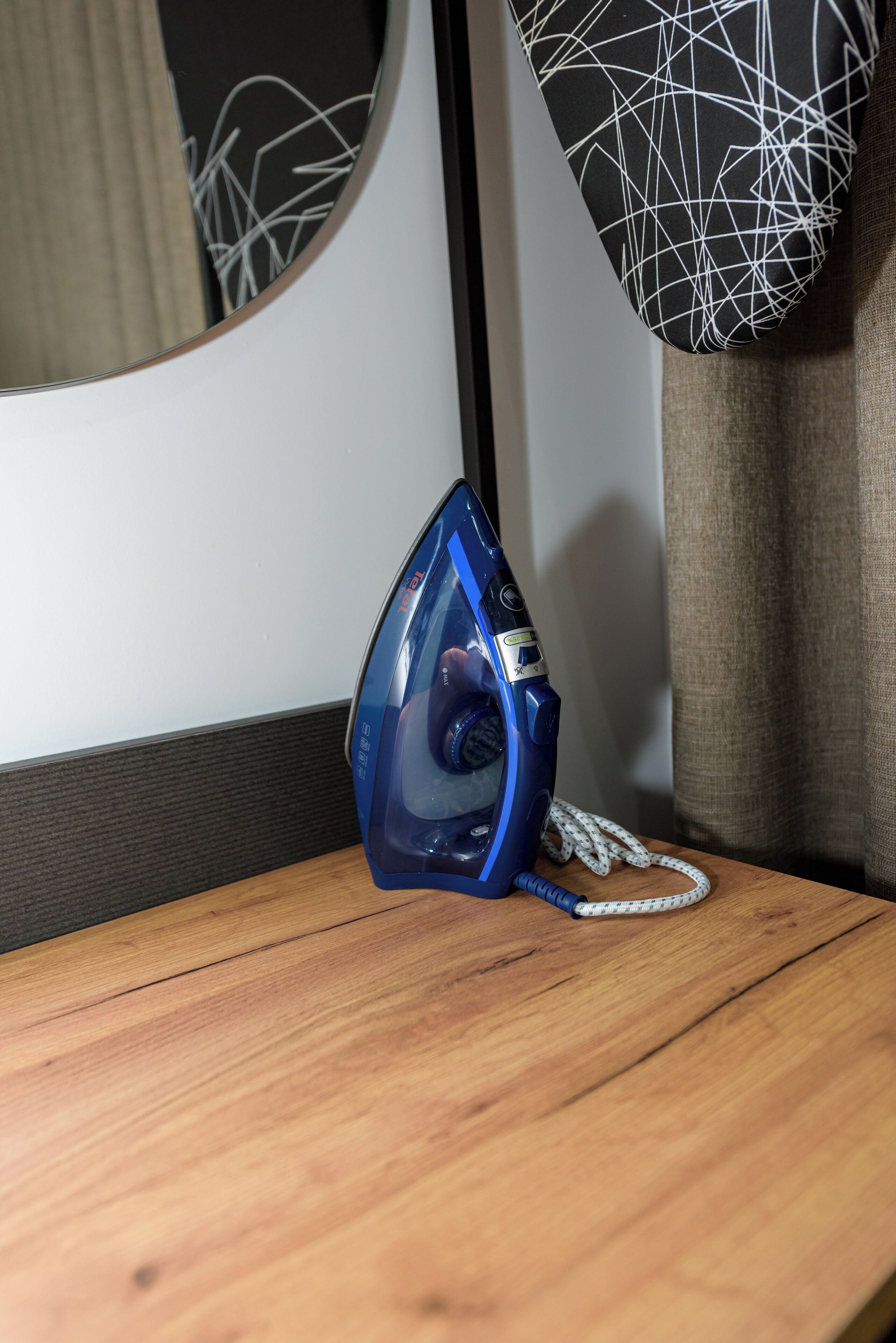 A blue iron on a wooden table next to a mirror with a black and white patterned pillow.