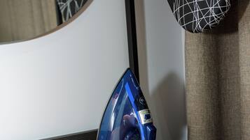 A blue iron on a wooden table next to a mirror with a black and white patterned pillow.