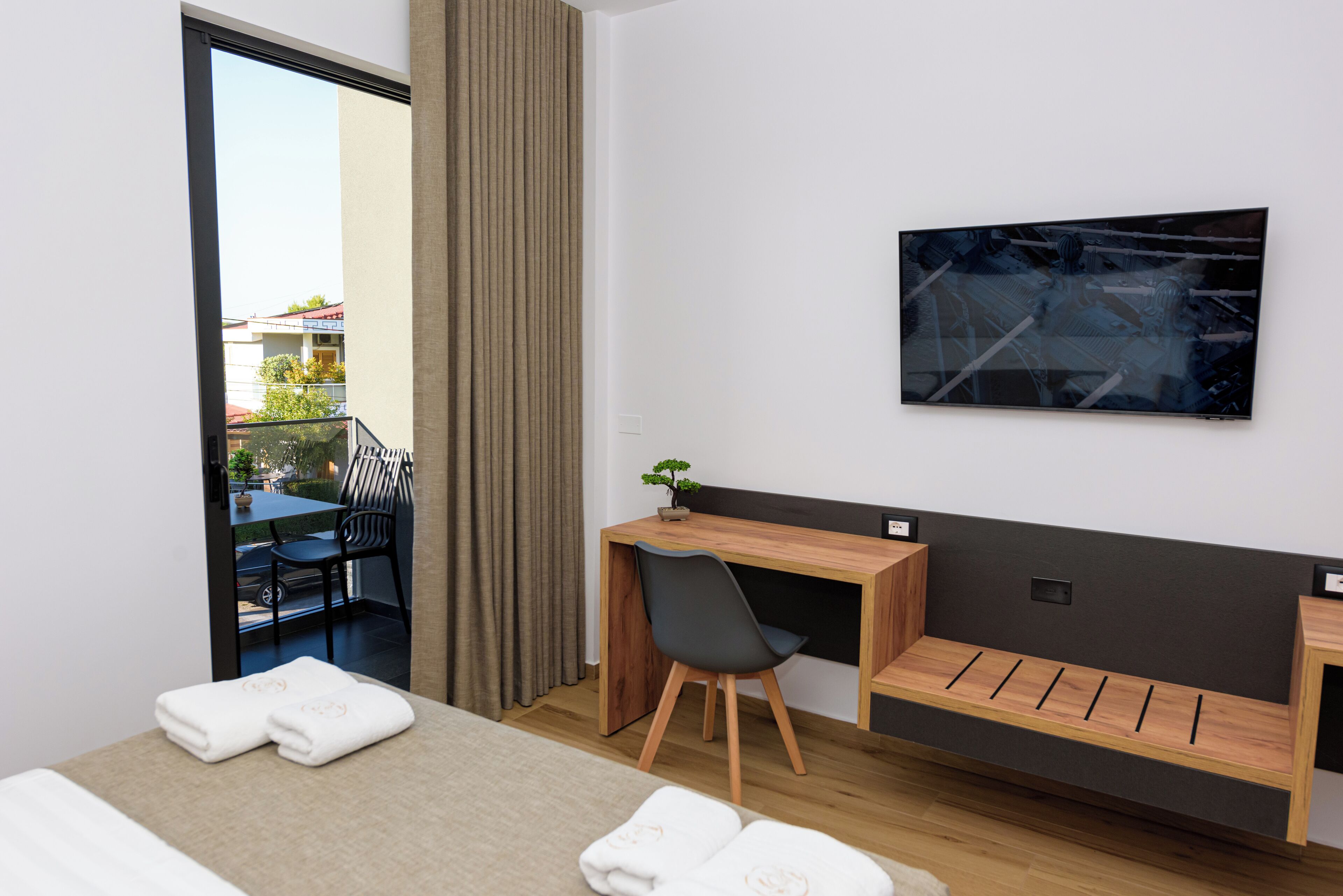 Ein modernes Hotelzimmer mit Bett, Schreibtisch, Stuhl und Blick auf den Außenbalkon.