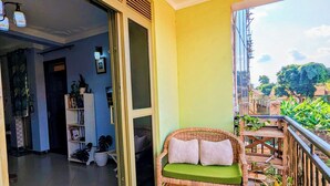 En balkon med en fletsofagruppe, krukker med planter og udsigt til grønne områder.