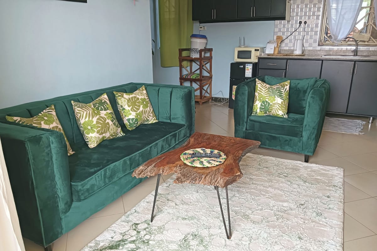 A living room with two green sofas, a wooden coffee table, and a kitchen in the background.