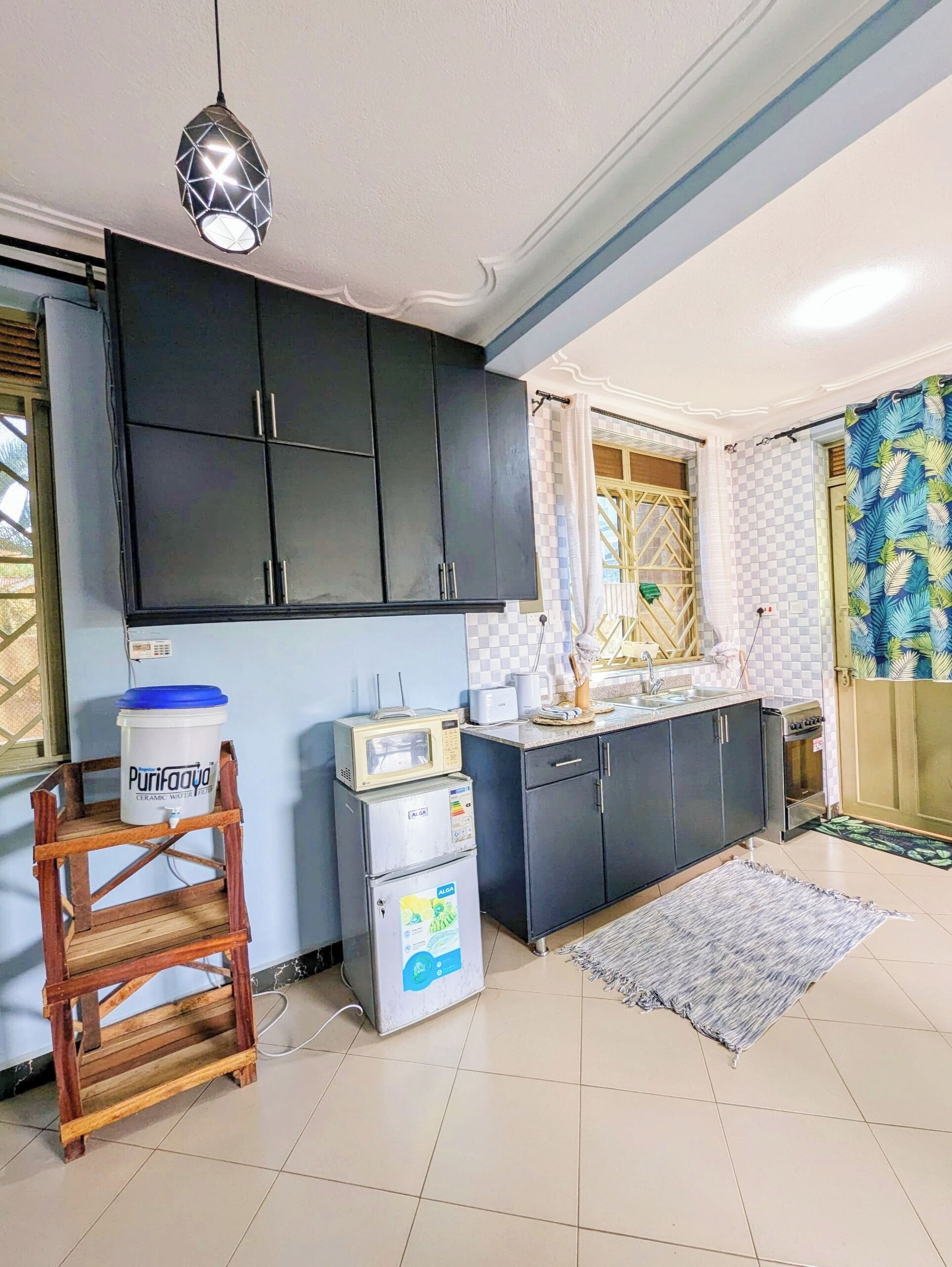 A compact kitchen with dark cabinets, a microwave, a small refrigerator, and a water dispenser.