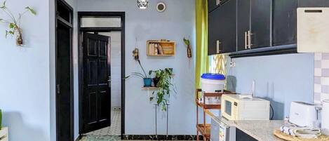 Una cocina moderna con armarios negros, un microondas y un lavamanos. Hay un taburete de madera y una planta colgante.