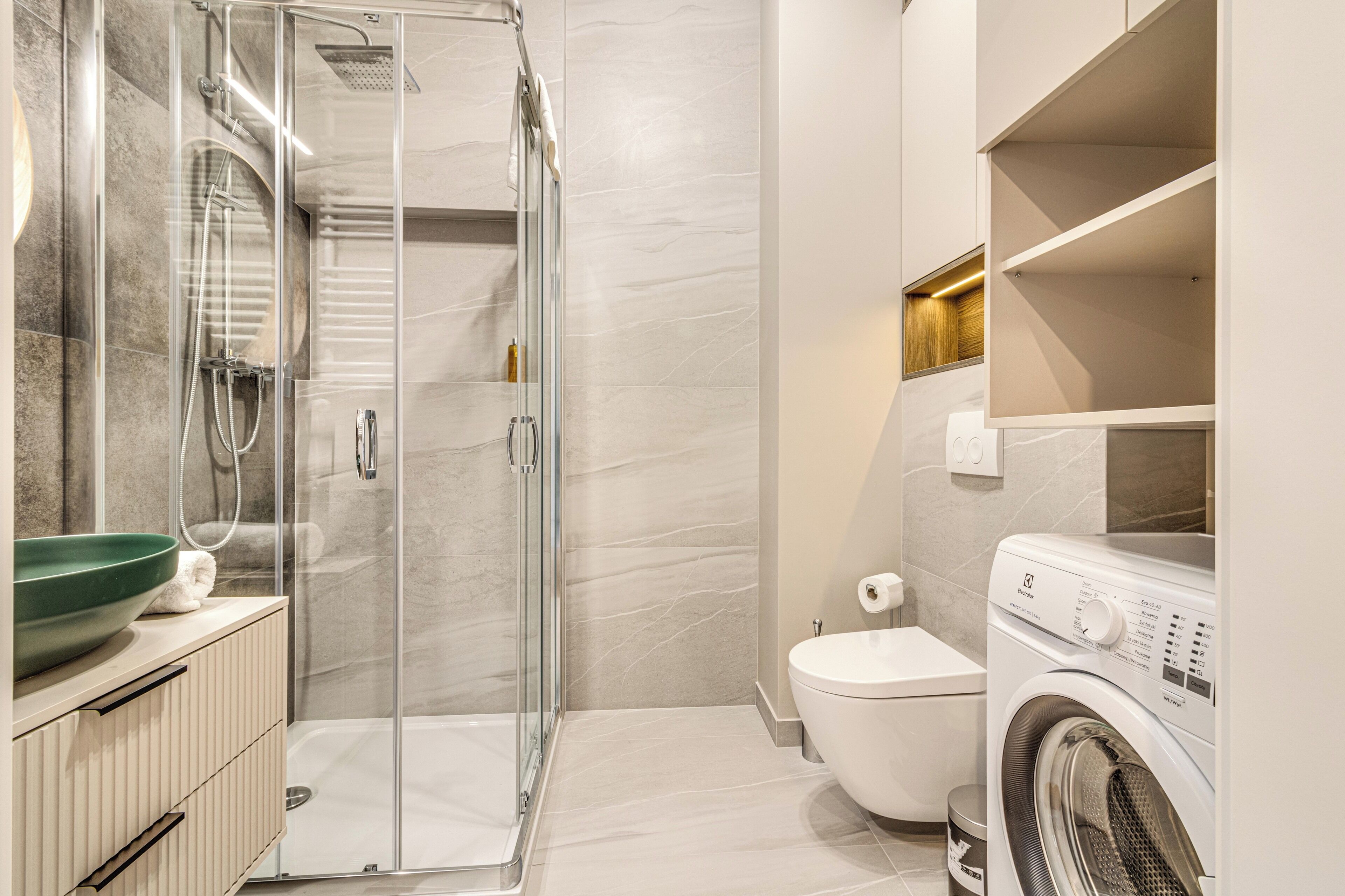 A modern bathroom with a glass-enclosed shower, a built-in washing machine, and a toilet.