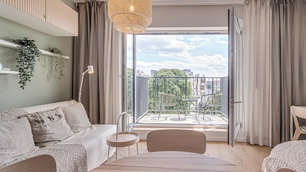 Una sala de estar moderna con un sofá, una mesita y un sillón. Hay un balcón con vistas a la ciudad y zonas verdes.