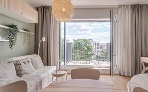A modern living room with a sofa, a small table, and a chair. There is a balcony with a view of the city and greenery. - RentPlanet - Apartamenty Dmowskiego (Wroclaw)