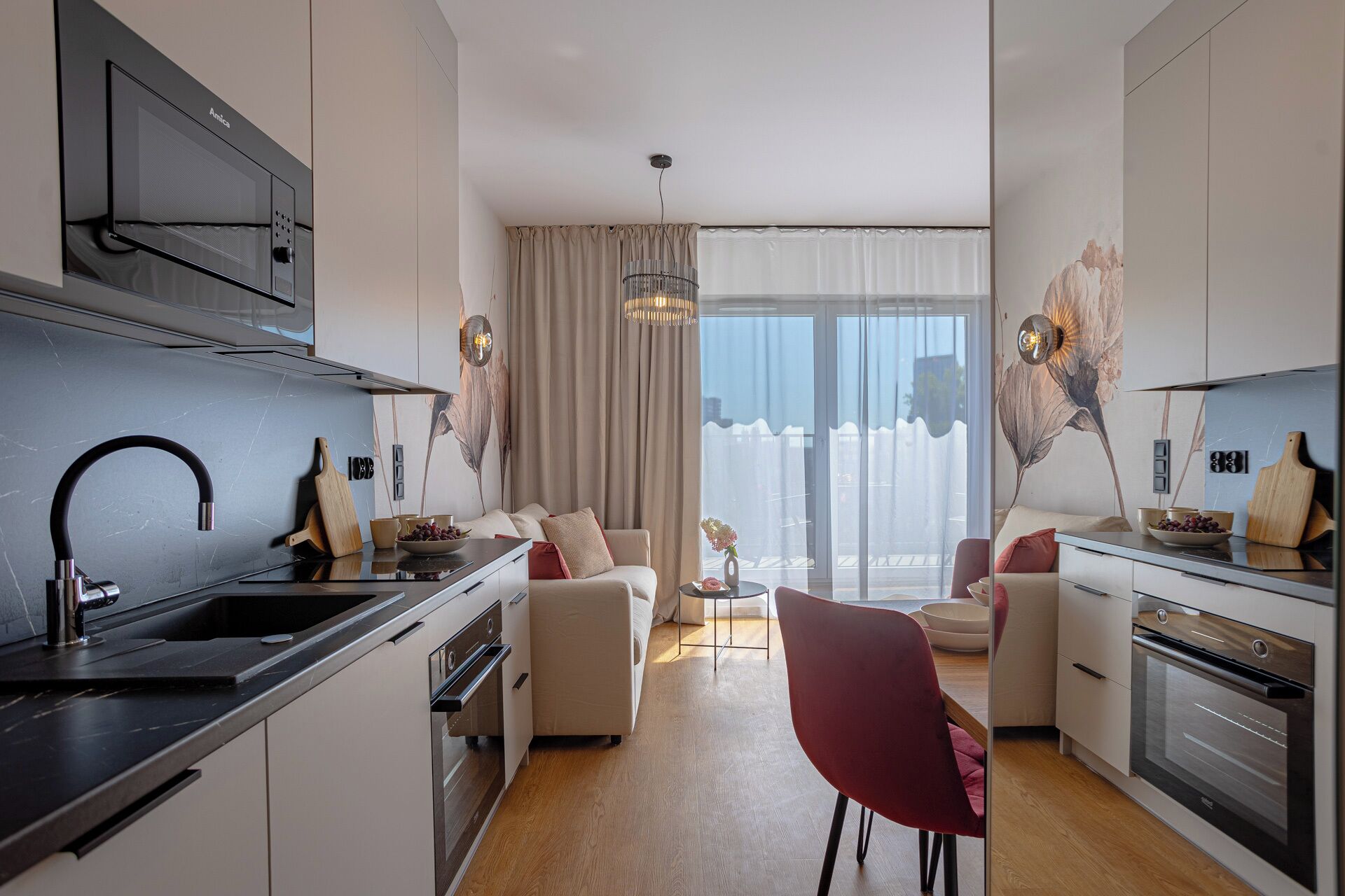 A modern kitchen with integrated appliances, a dining area with a red chair, and a large window with curtains.
