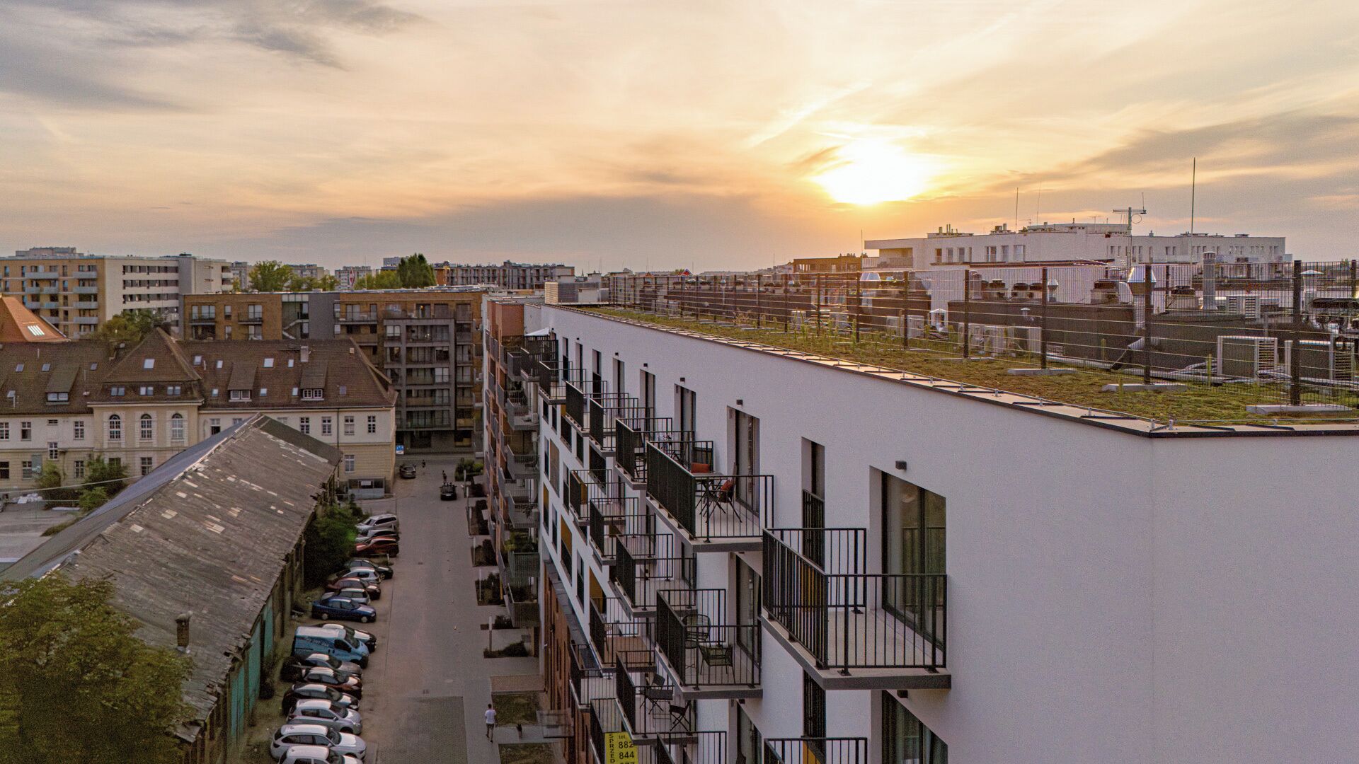Un edifici modern amb múltiples balcons, una zona d'aparcament i un cel ocre al fons.
