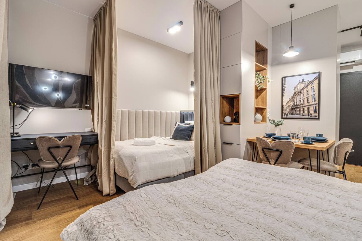A modern hotel room with a large bed, a desk, a chair, and a dining area.