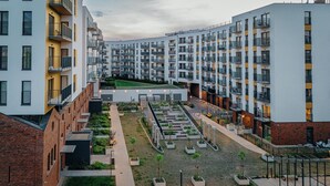 Un moderno complejo de apartamentos con varios balcones, un patio central con jardineras y un edificio de ladrillo en un lateral.