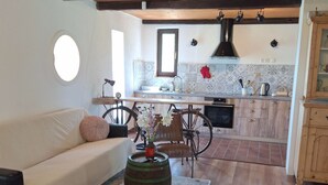 A cozy living room with a sofa, a vintage suitcase, and a rustic coffee table. A kitchen with wooden cabinets and a tiled backsplash is visible in the background. - Holiday Home Nadira (Erdut)