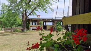 A rustic building with a wooden deck, surrounded by a grassy area and trees. - Holiday Home Nadira (Erdut)