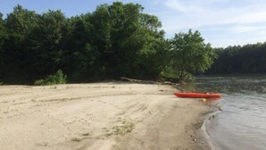 A sandy beach with a red kayak near the water's edge, surrounded by dense green trees. - Holiday Home Nadira (Erdut)
