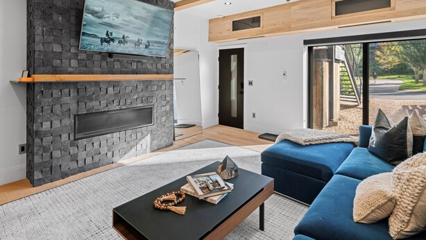 Ein modernes Wohnzimmer mit Kamin aus Stein, einem Flachbildfernseher und einem blauen Sofa.