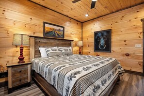 A wooden-paneled bedroom with a large bed, two bedside lamps, a ceiling fan, and framed artwork on the walls. - Panoramic Paradise Splash – A Splash of Fun All Around (SEVIERVILLE)