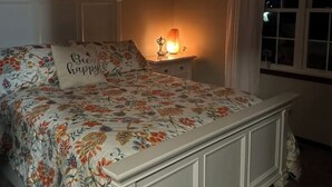 Een slaapkamer met een bed, nachtkastje, lamp, raam met gordijnen en een plafondventilator.