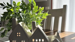Een keramieken plantenpot in de vorm van een huis, met een plant op een geruit tafelkleed.