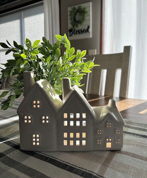 A ceramic house-shaped planter with a plant on a checkered tablecloth.