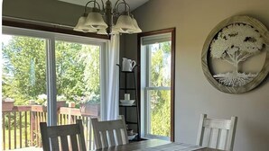 Een eethoek met een houten tafel en bankjes, grote ramen met uitzicht op groen, en een kunstwerk van een boom aan de muur.