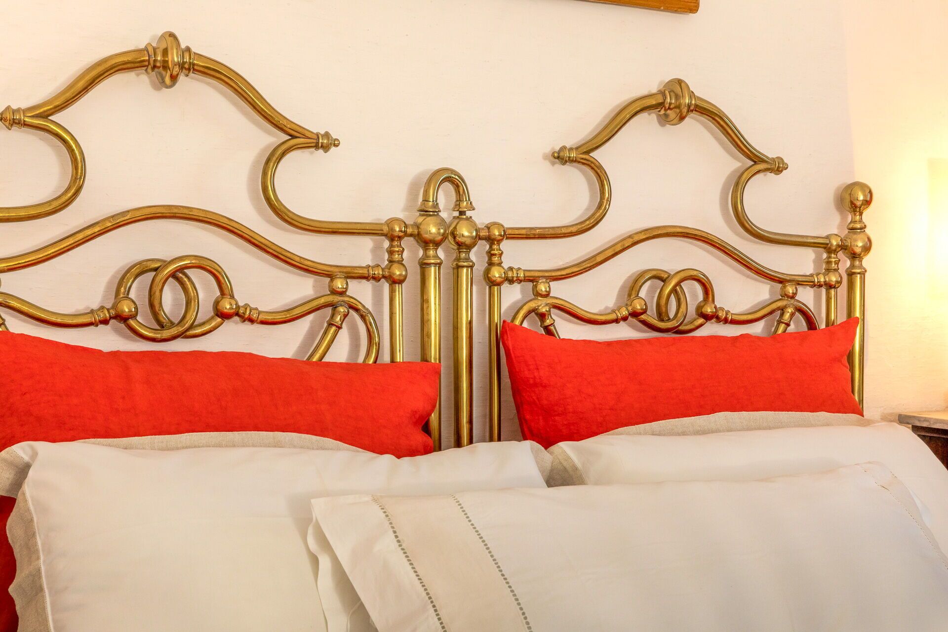 A bed with a gold metal frame, two red pillows, and white bedding.