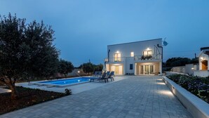 Ein modernes, zweistöckiges Haus mit Swimmingpool, Sitzgelegenheiten im Freien und einem gepflegten Garten.