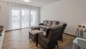 Ein geräumiges Wohnzimmer mit einer Couch, zwei Sesseln und einem Couchtisch. Eine Glastür verschiebt sich zu einem Außenbereich.