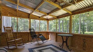 A covered porch with wooden flooring, a rocking chair, a folding chair, and a small table.