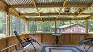 A covered porch with wooden chairs, a small table, and a patterned rug.