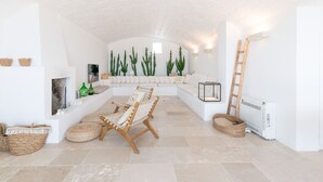 A spacious room with a white ceiling, a large window, a white sofa, a wooden chair, and several woven baskets.