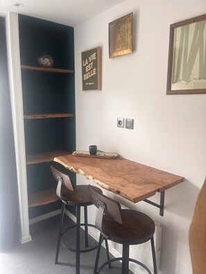 A dining area with a wooden table, two chairs, and a shelf unit.
