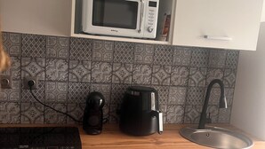 Una cocina con microondas, cafetera y hervidor sobre la encimera, un lavabo y azulejos decorativos en el salpicadero.