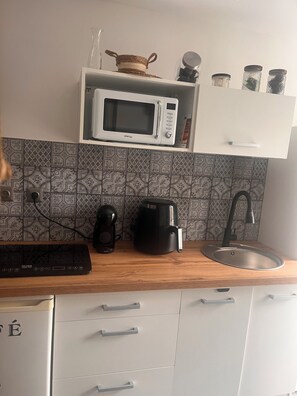 A kitchen with a microwave, coffee maker, and kettle on the counter, a sink, and patterned backsplash tiles.
