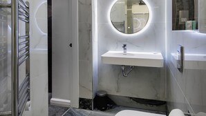 Ett modernt badrum med ett marmorgolv, en rund spegel, en vit handfat och en toalett.